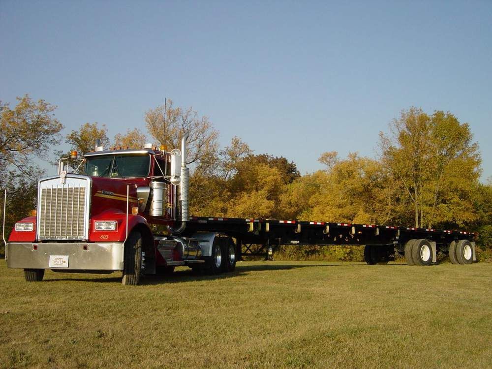 A red semi truck is parked in a grassy field