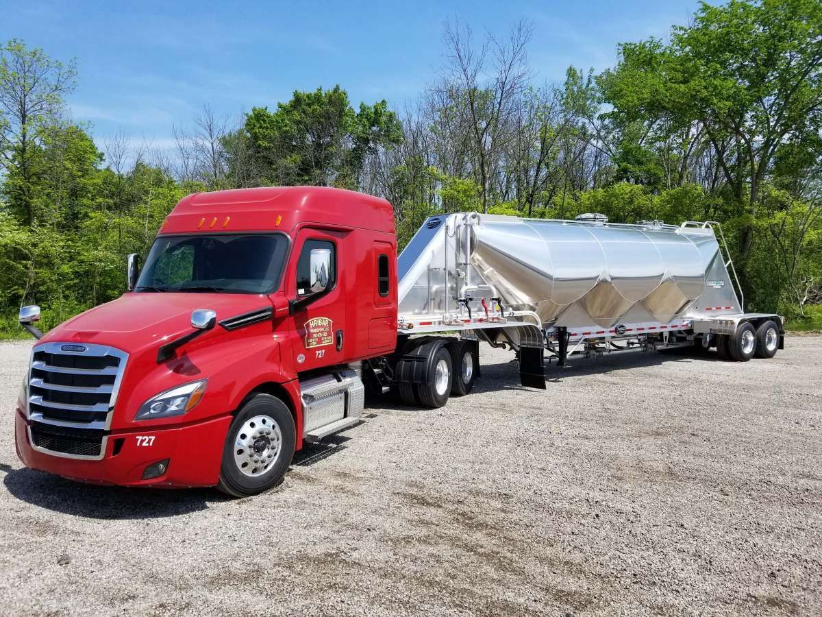 A red semi truck with a trailer attached to it is parked in a gravel lot.
