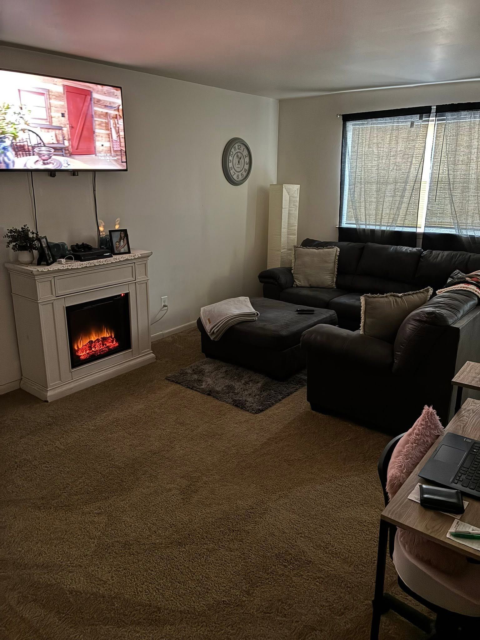 Cozy living room with wall-mounted TV, electric fireplace, dark sectional sofa, and large window.