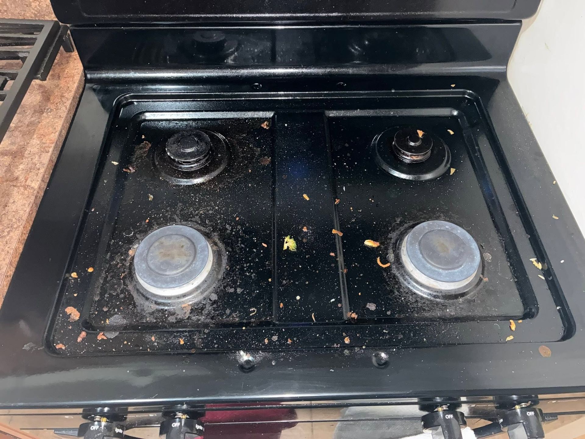 Black stovetop with four burners, scattered food splatters, and a dirty cooktop surface