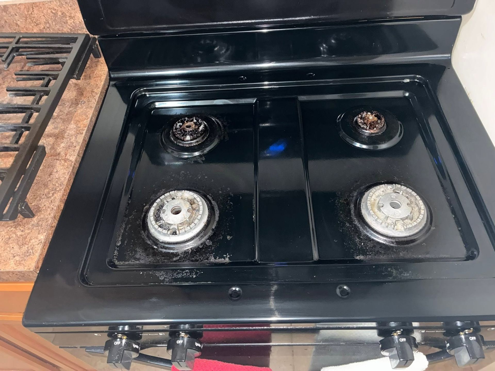 Black gas stove with four burners, two front burner caps removed, in a kitchen.