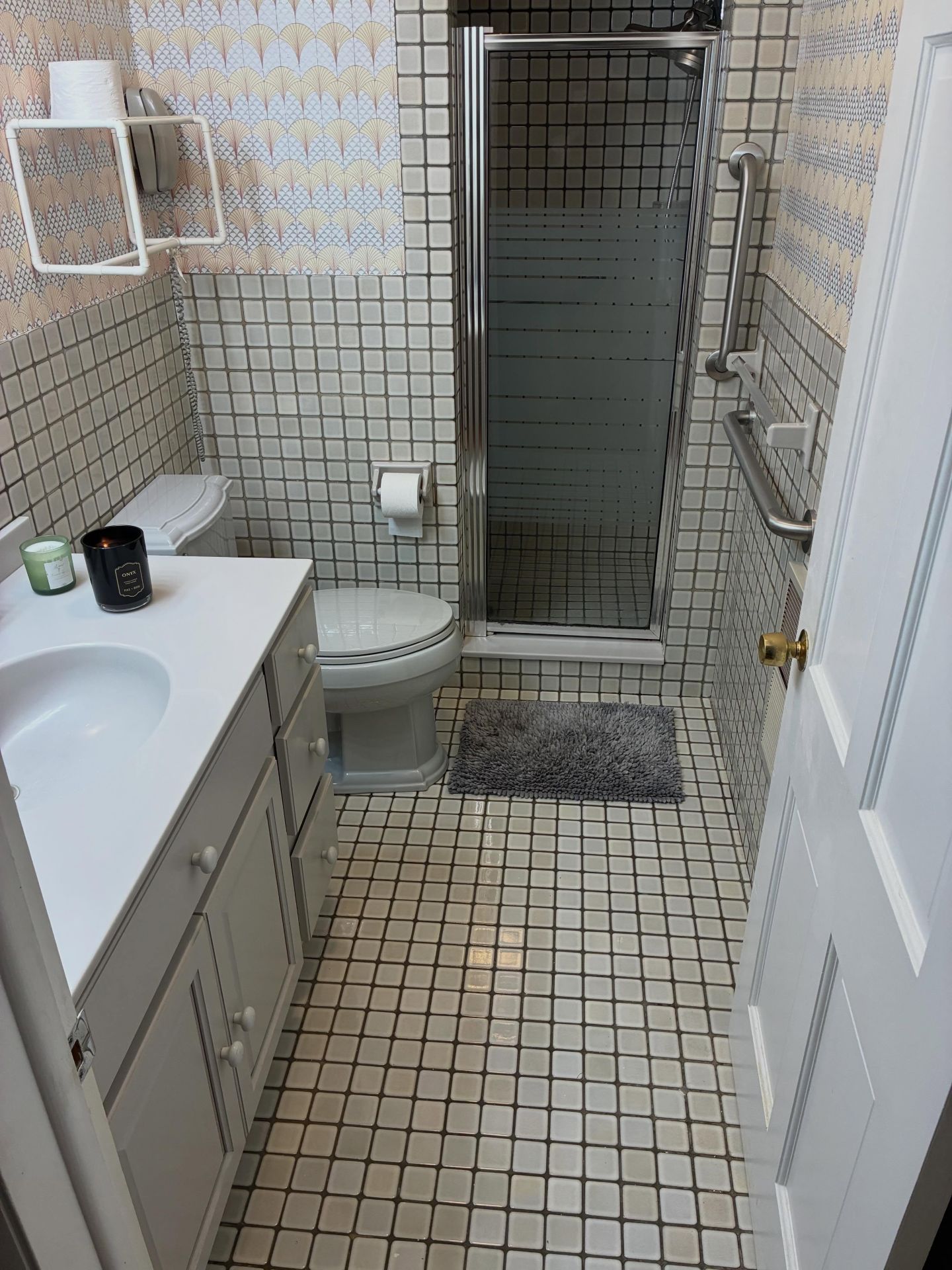 Small bathroom with white tile, sink, toilet, shower stall, and bath mat.