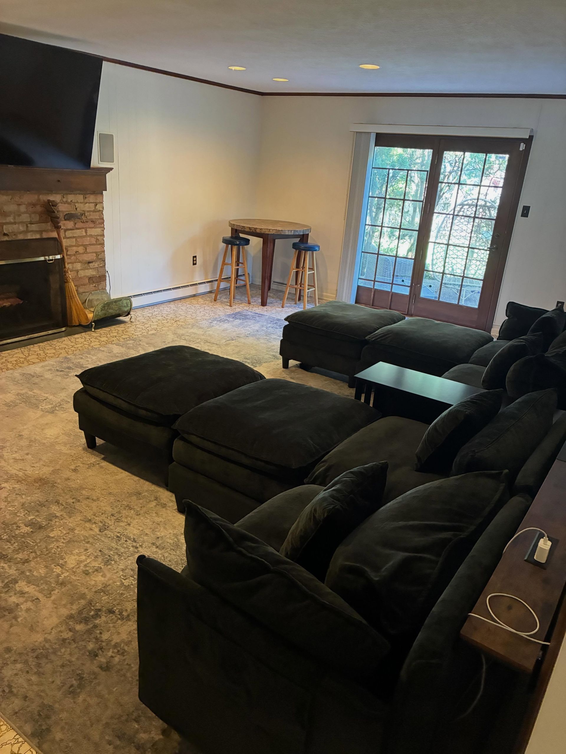 Living room with dark sectional sofas, stone fireplace, and French doors opening to a wooded view