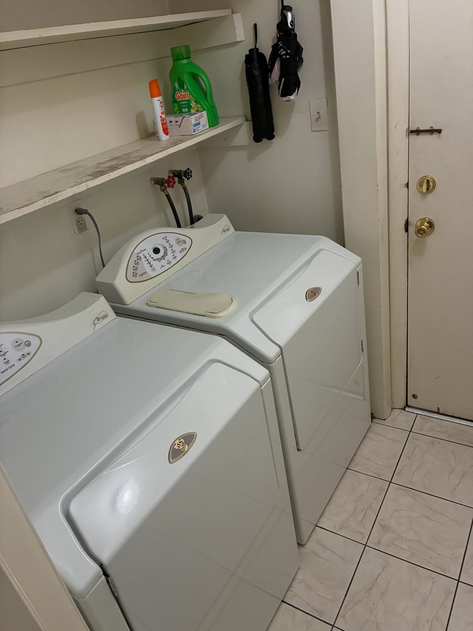 Laundry room with two white top-load washer/dryer units and a shelf of cleaning supplies