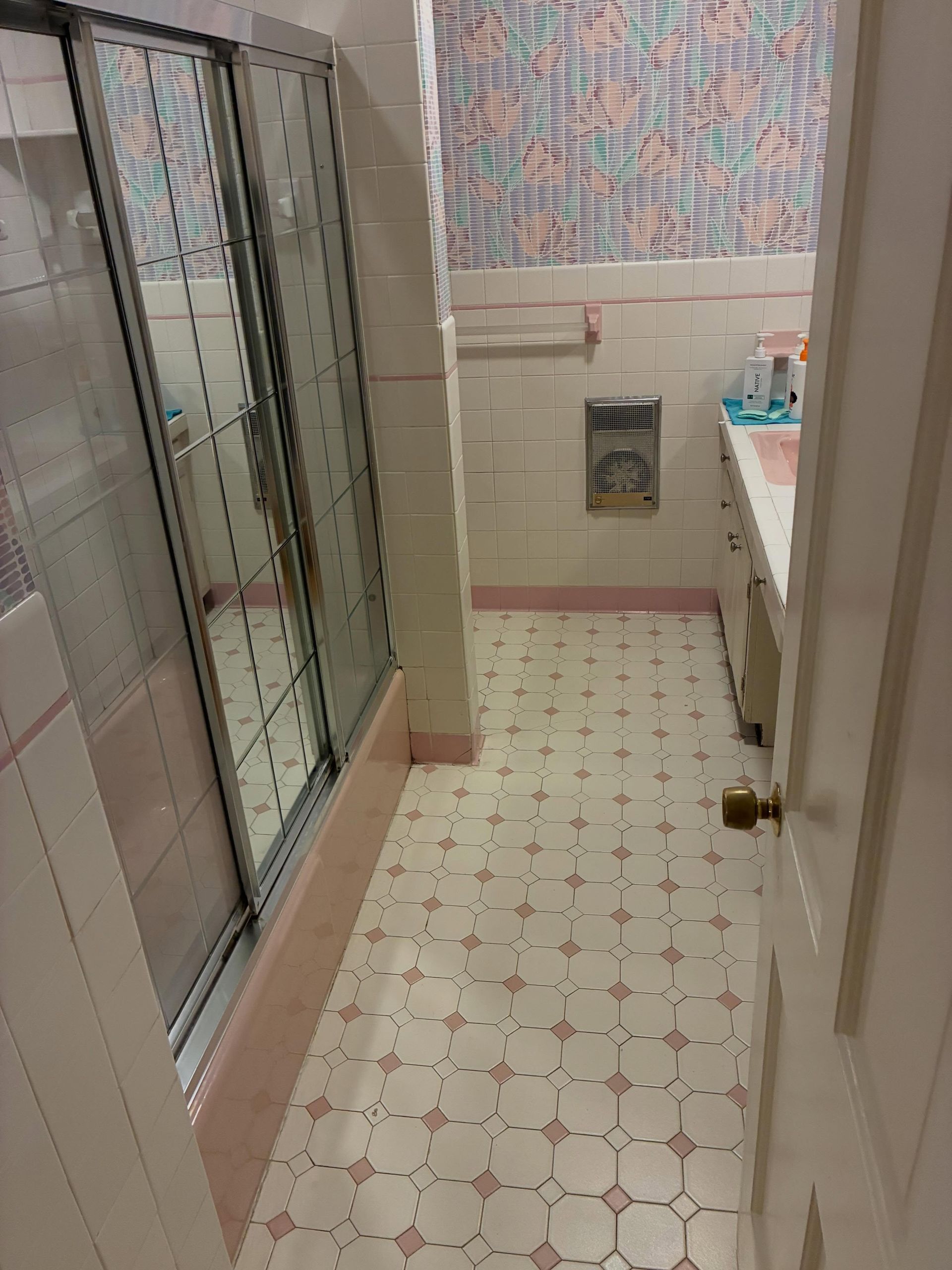 Small bathroom with glass shower, beige tile, patterned floor, and sink vanity.