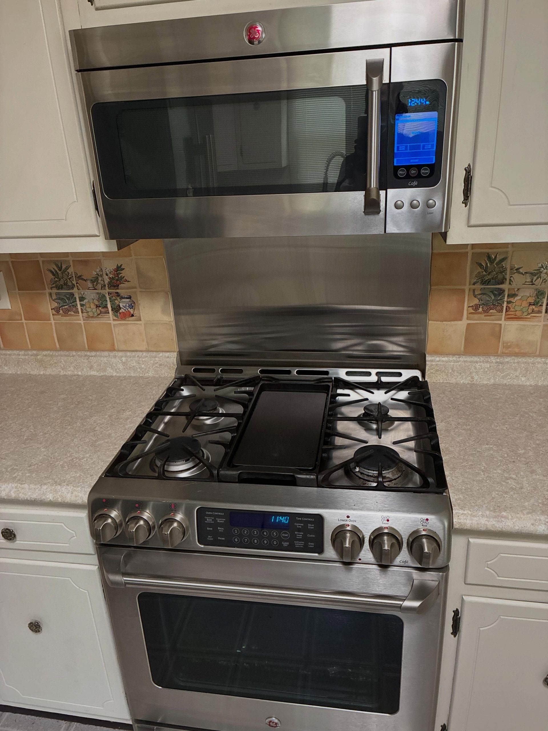 Stainless steel gas range with built-in microwave in a tiled kitchen.