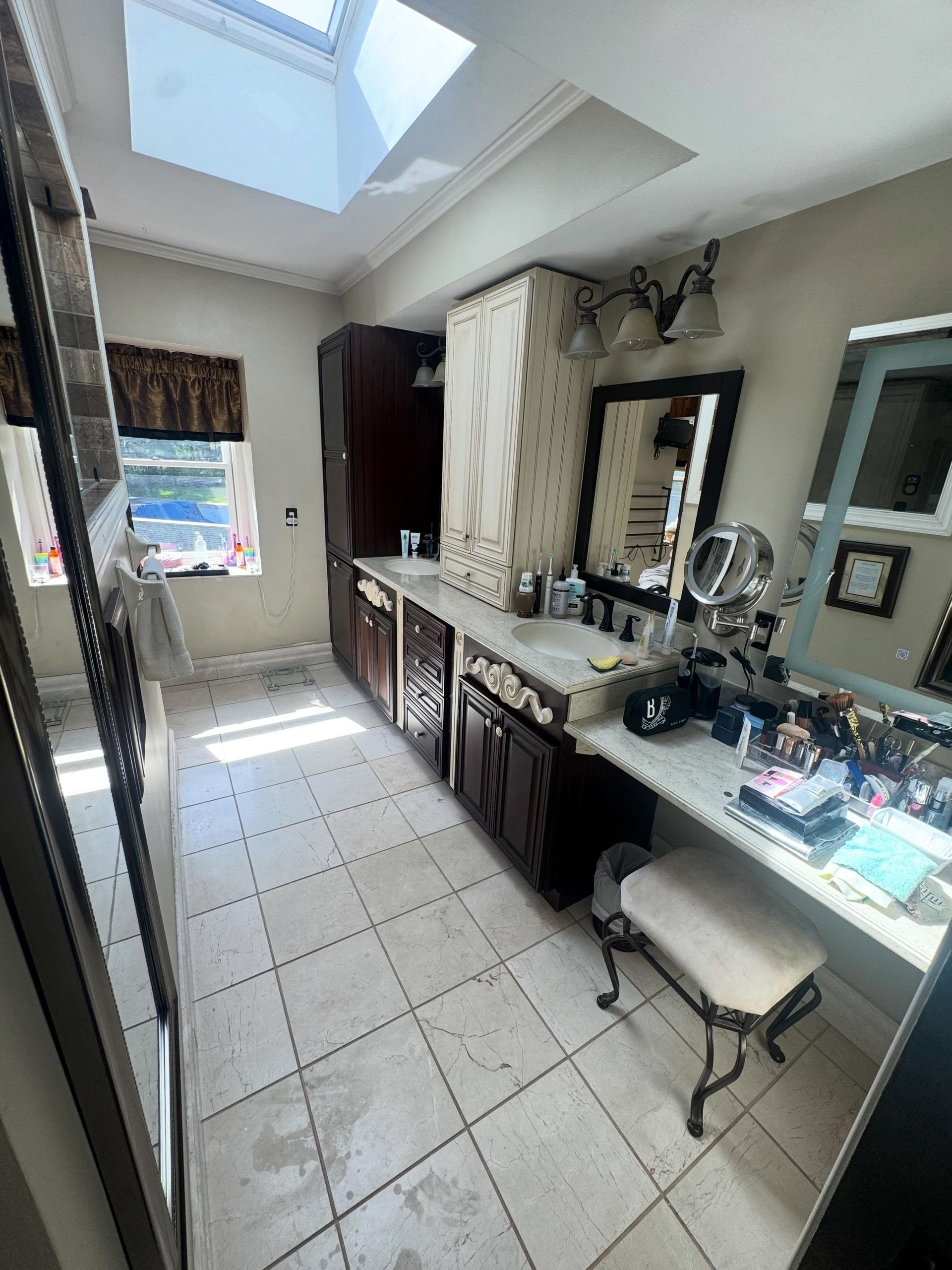 Bright bathroom with skylight, double vanity, mirrors, and white tiled floor