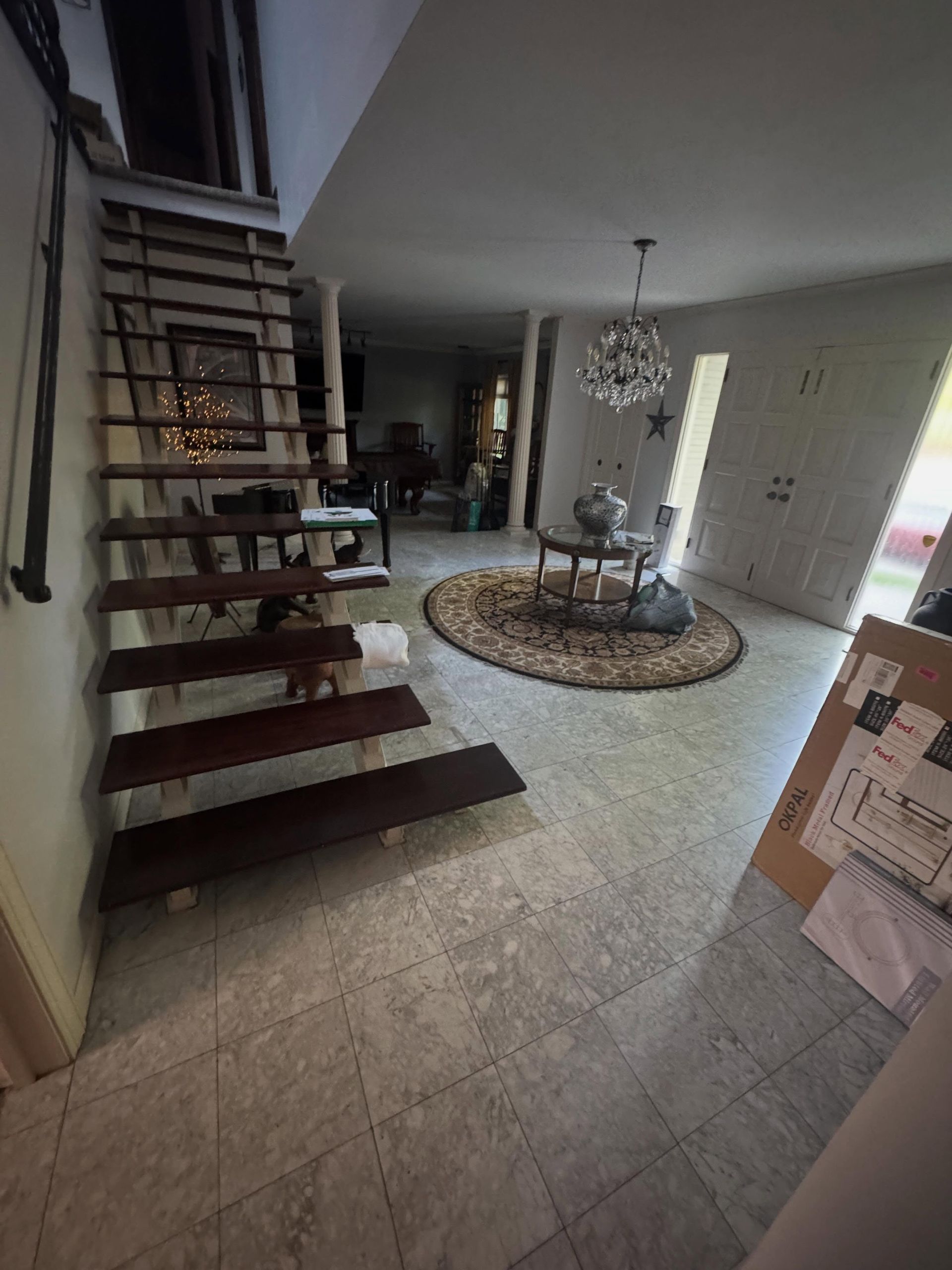 Modern home interior with floating staircase, tiled floor, chandelier, and round rug near a bright window
