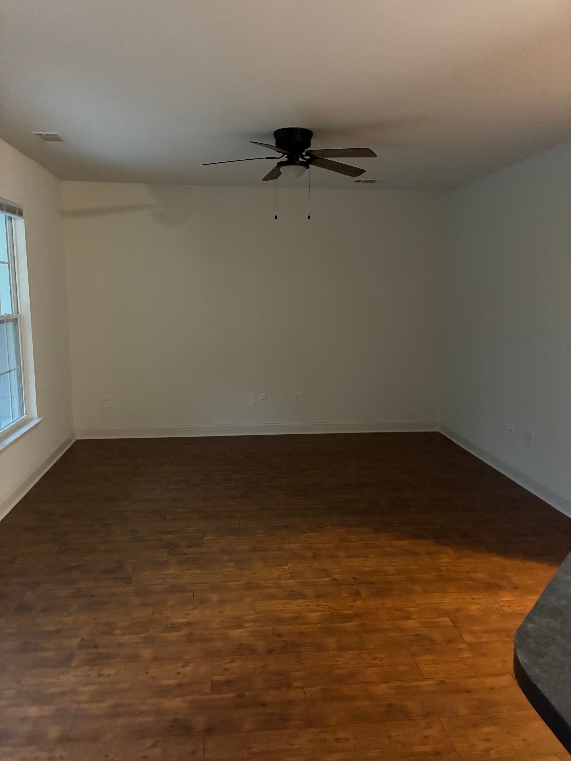 Empty room with white walls, wood floor, and a ceiling fan near a window