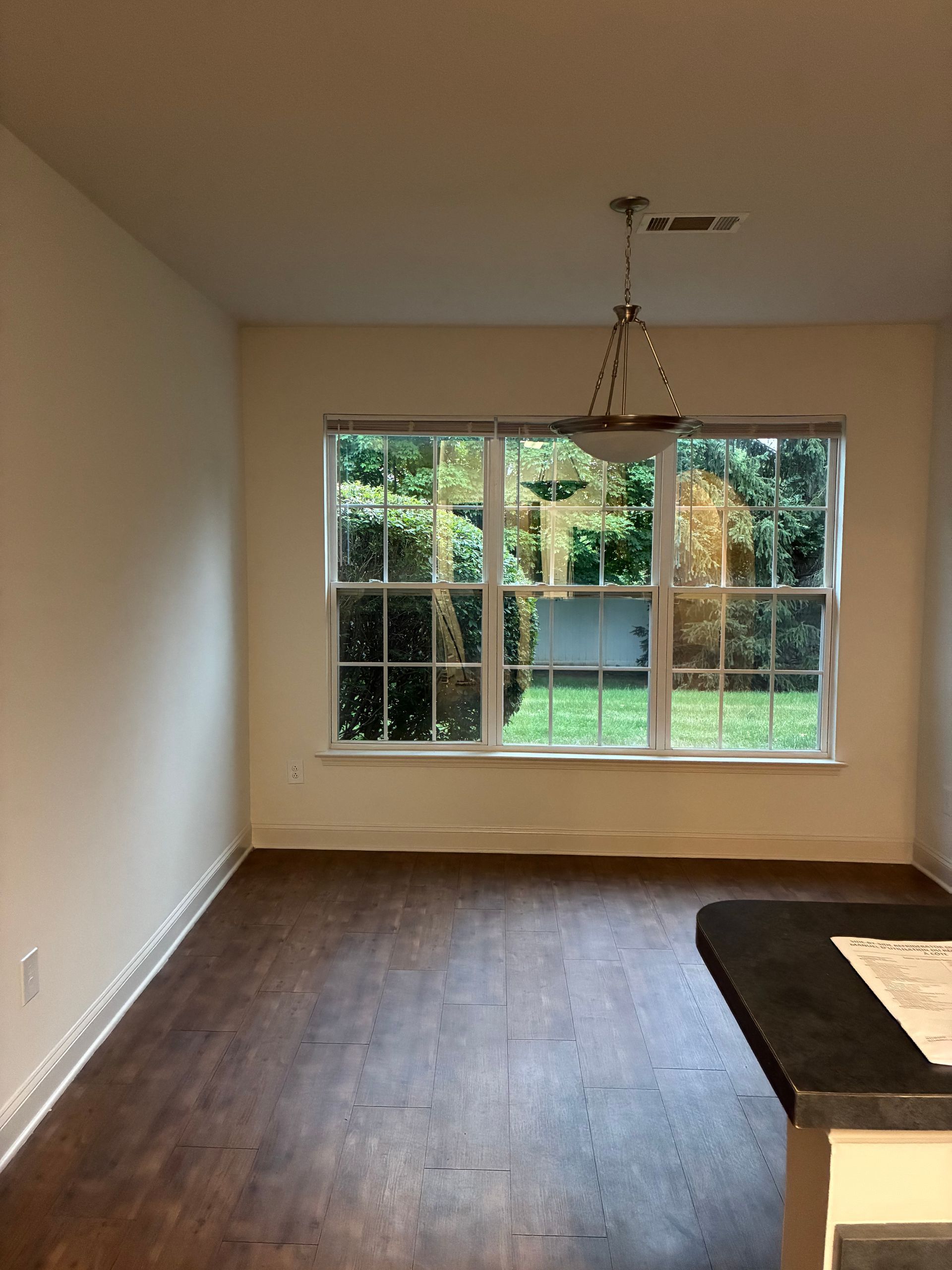 Empty dining room with dark wood floor, large window, and chandelier, viewed from kitchen counter