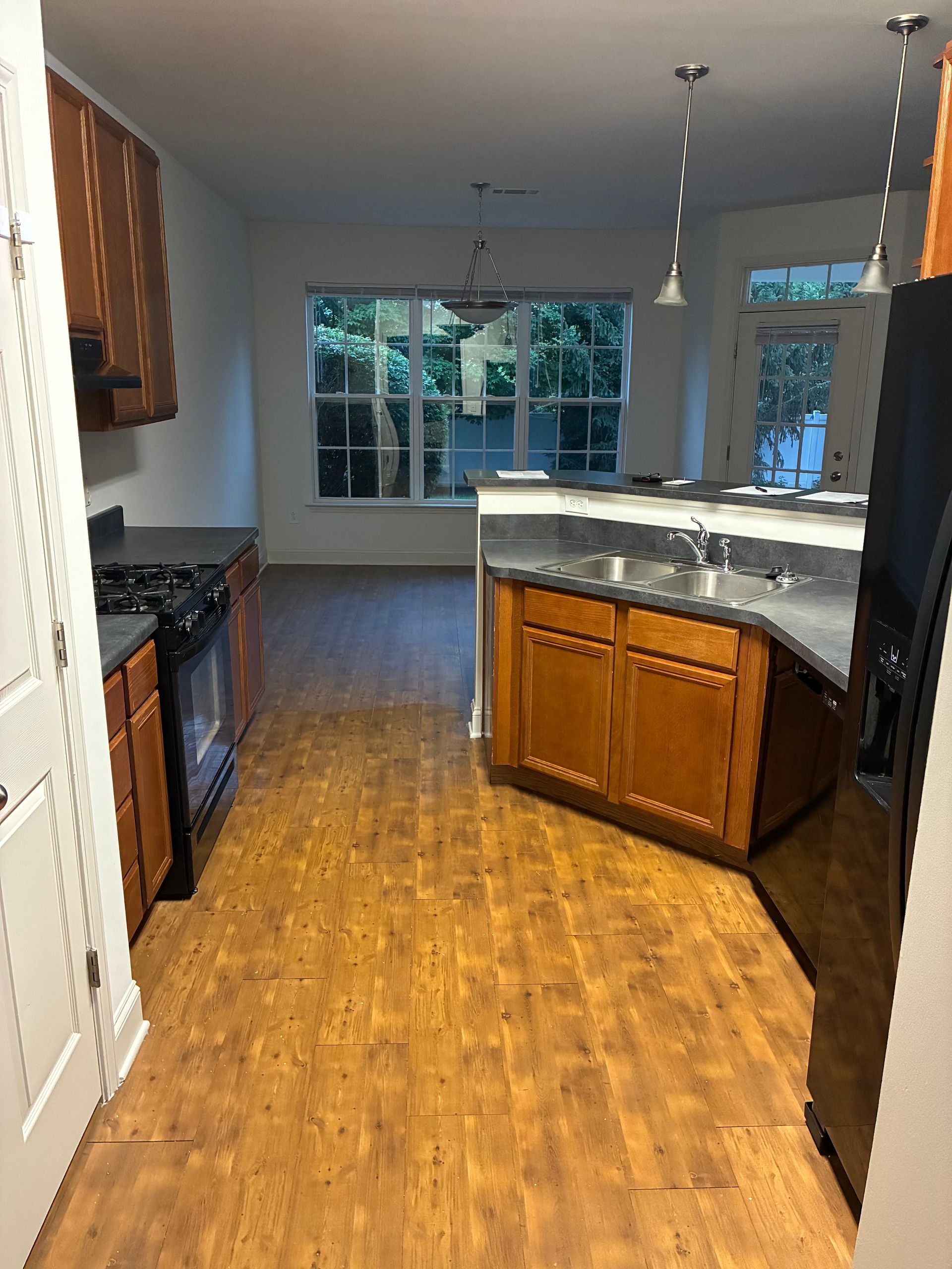 Empty kitchen with wood floors, white cabinets, black appliances, and a large island under pendant lights.