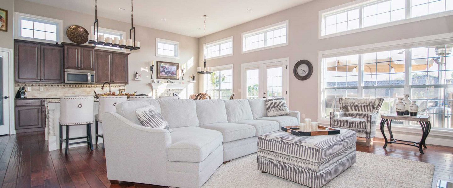 Bright open living room with white sofa, patterned ottoman, and kitchen area in the background