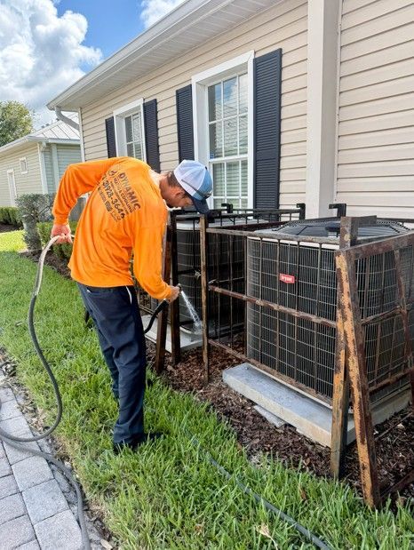 Man in orange shirt washing an AC unit outside a house.