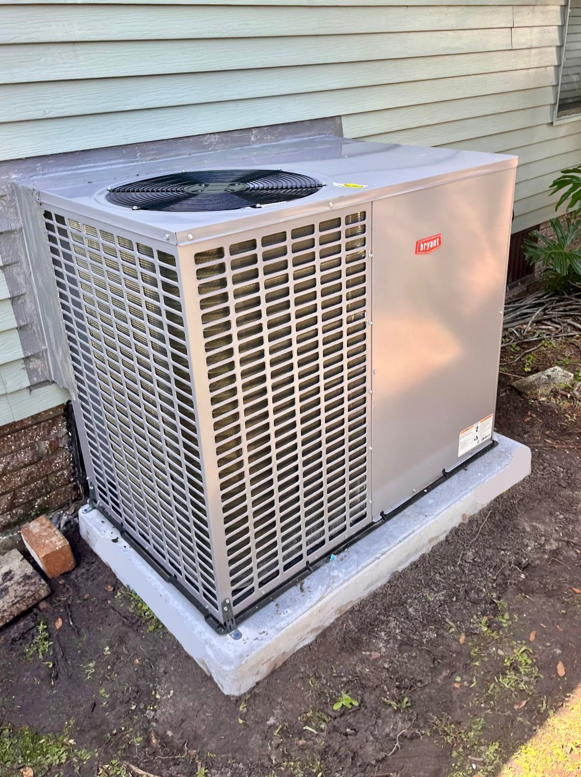 Gray air conditioning unit on a concrete pad next to a building.