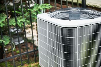 Air conditioning unit outside next to a fence and greenery.