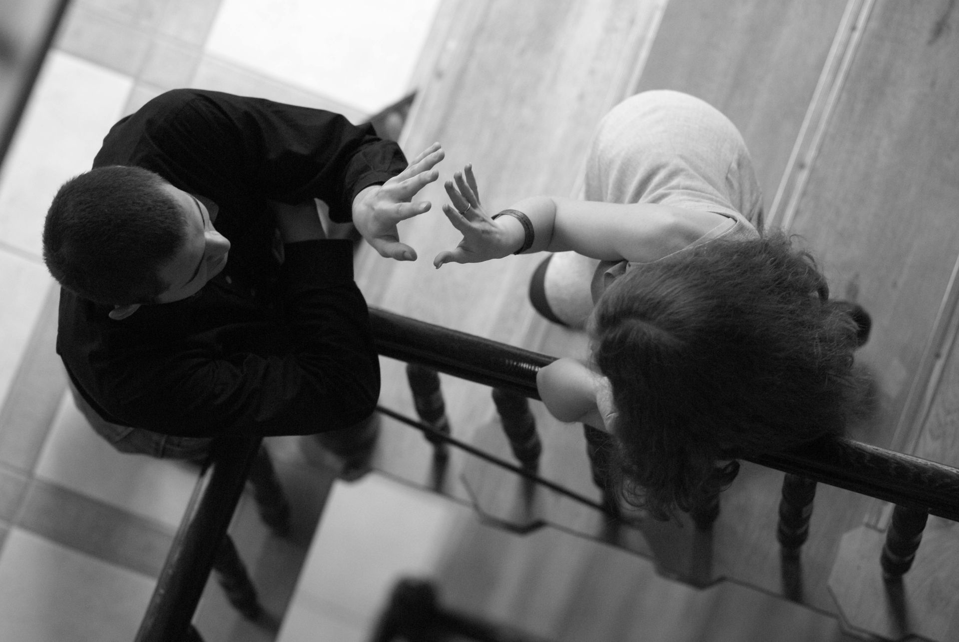 Two people reaching toward each other across a stair railing in a black-and-white overhead photo