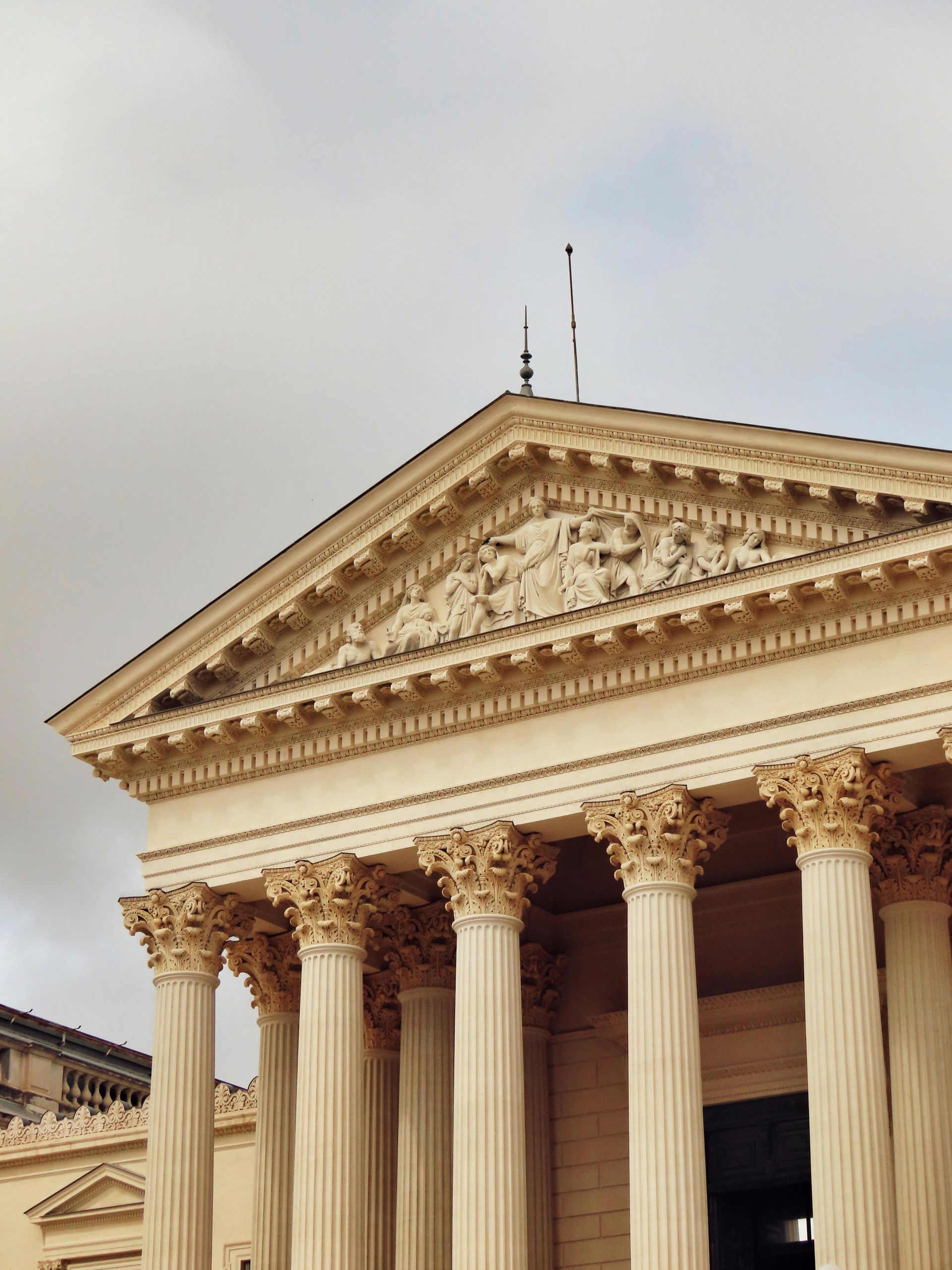 Classical stone temple facade with columns and a triangular pediment against a cloudy sky