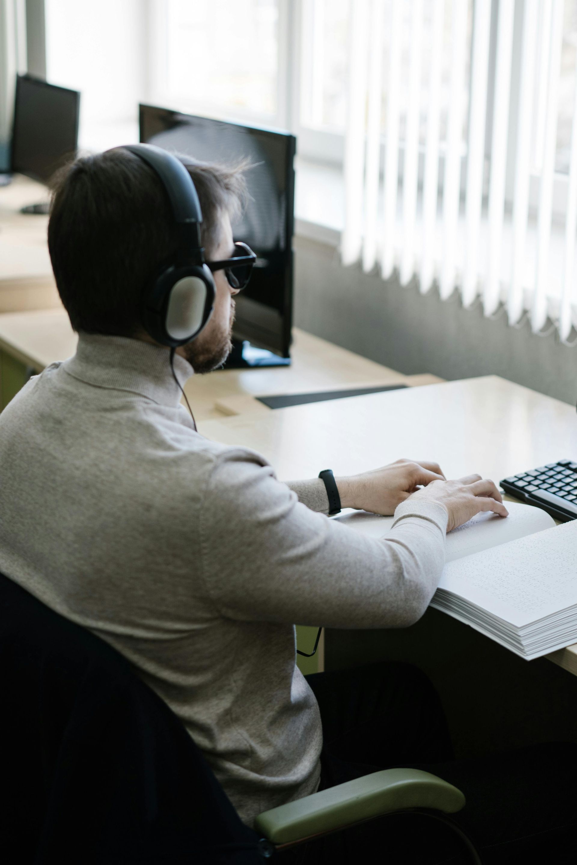 Person wearing headphones works at a desk with a computer in a bright office