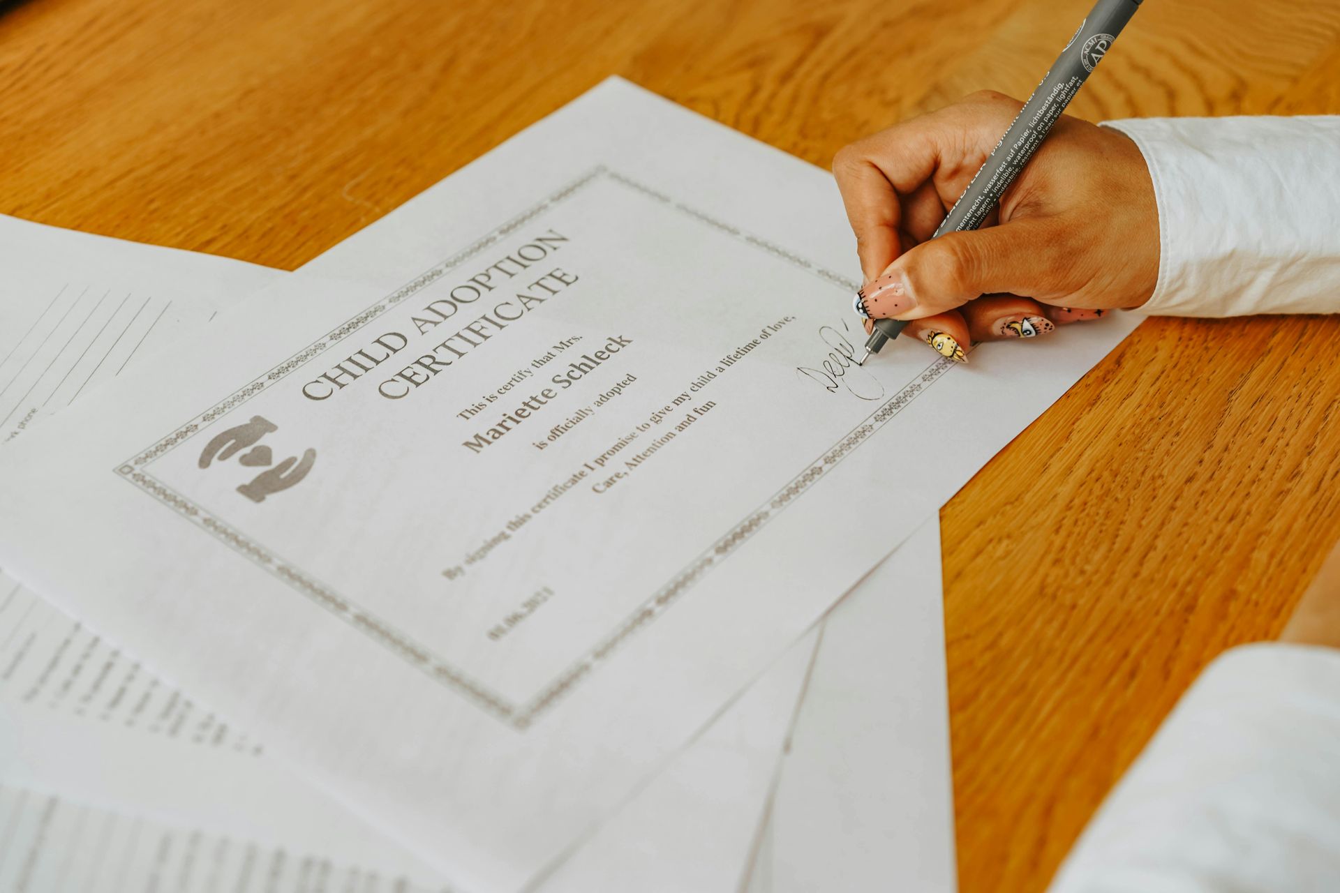 Hand signing a certificate on a wooden desk with papers nearby