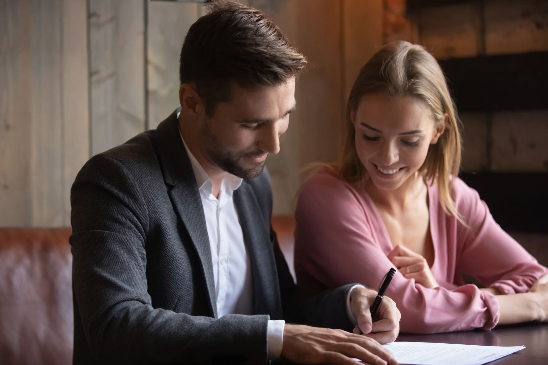 Two people reviewing documents at a table, smiling and discussing notes in a warm indoor setting.
