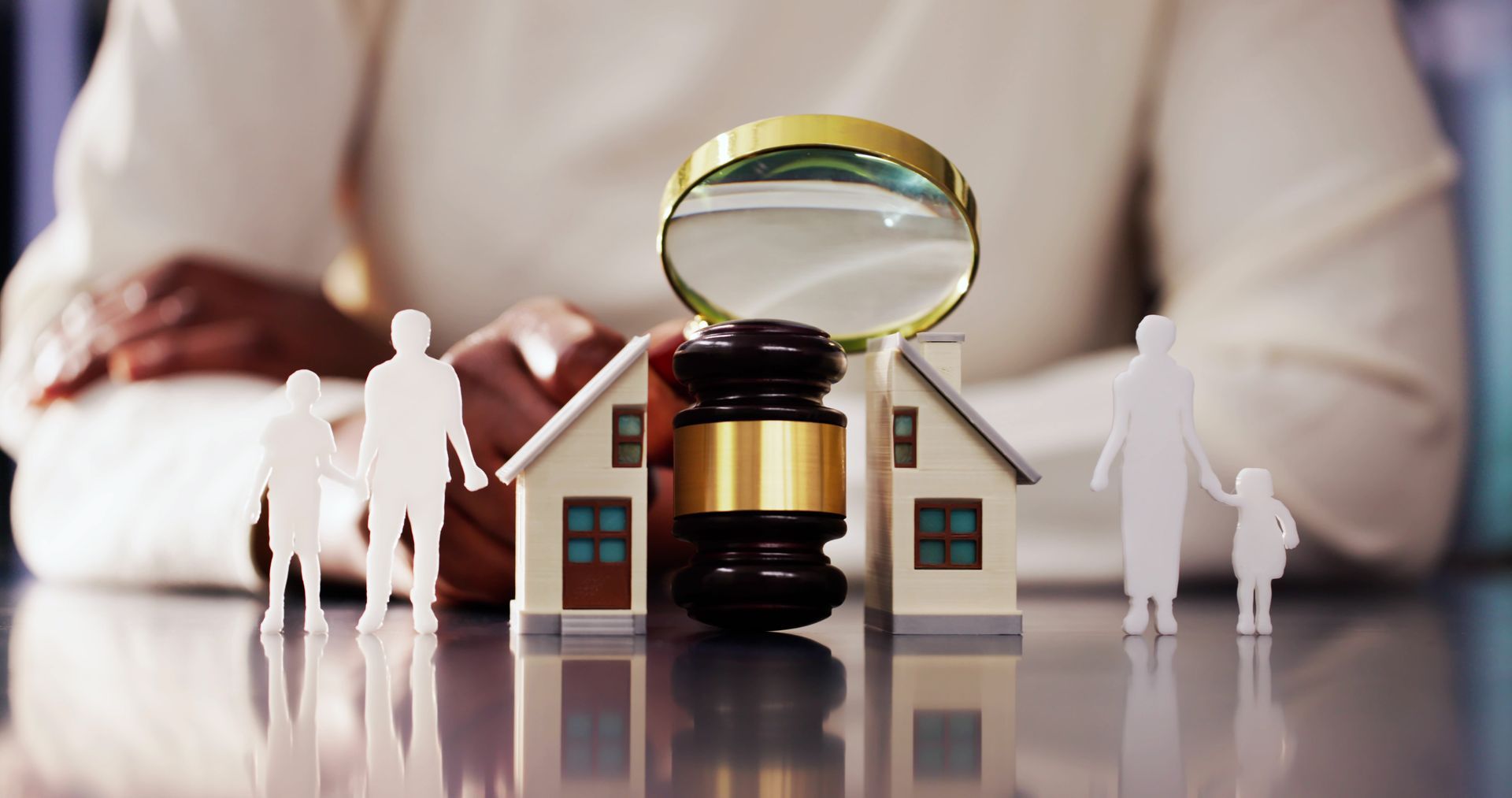 House model and gavel under magnifying glass, with small figures standing beside it on a reflective surface