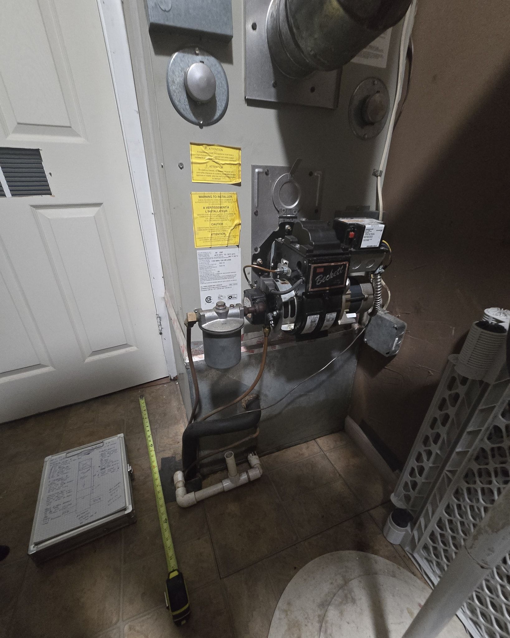 Gas furnace in a utility room. Yellow labels on side.  A/C vent on the wall on the left.