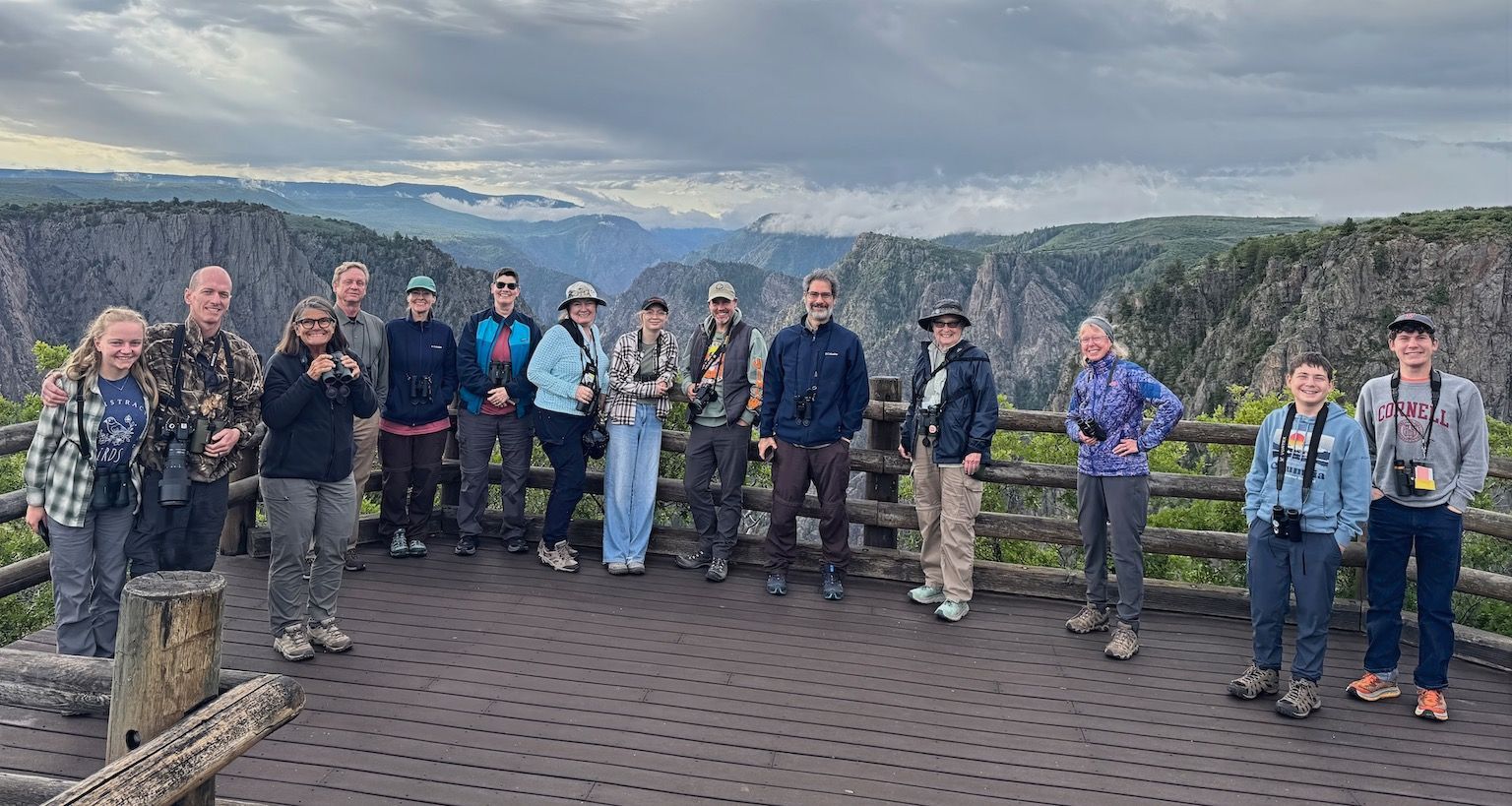 Group of tourists posing on a lookout platform with canyon cliffs and cloudy sky in the background