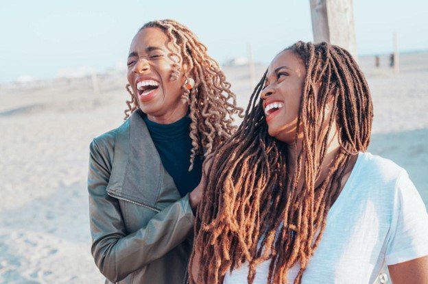 Two women smile and laugh together on a beach Two women smile and laugh together on a beach