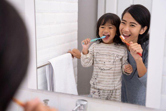 A mother and daughter brush their teeth together in front of the bathroom mirror A mother and daughter brush their teeth together in front of the bathroom mirror