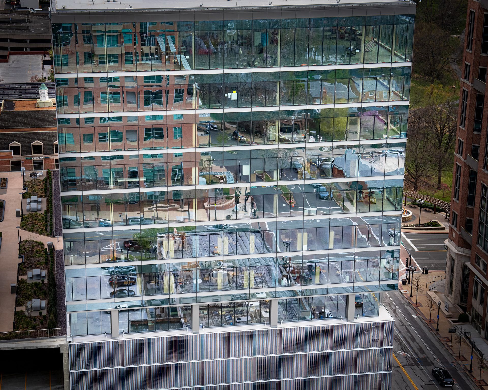 Glass skyscraper reflecting surrounding buildings and street.