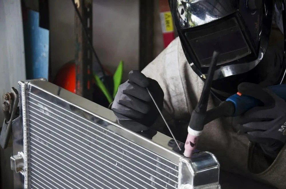A Man Wearing a Welding Helmet Is Welding a Radiator — Radiator Doctor In Pialba, QLD