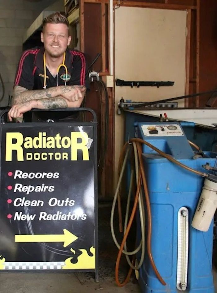 A Man Leaning on A Sign that Says Radiator Doctor — Radiator Doctor In Pialba, QLD