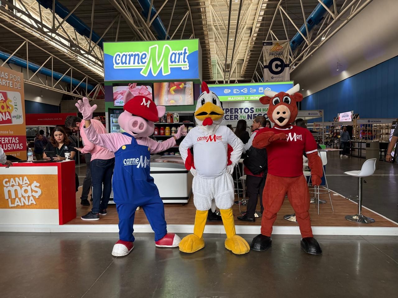 Tres personajes disfrazados (cerdo, pollo, toro) posando frente a un stand de 