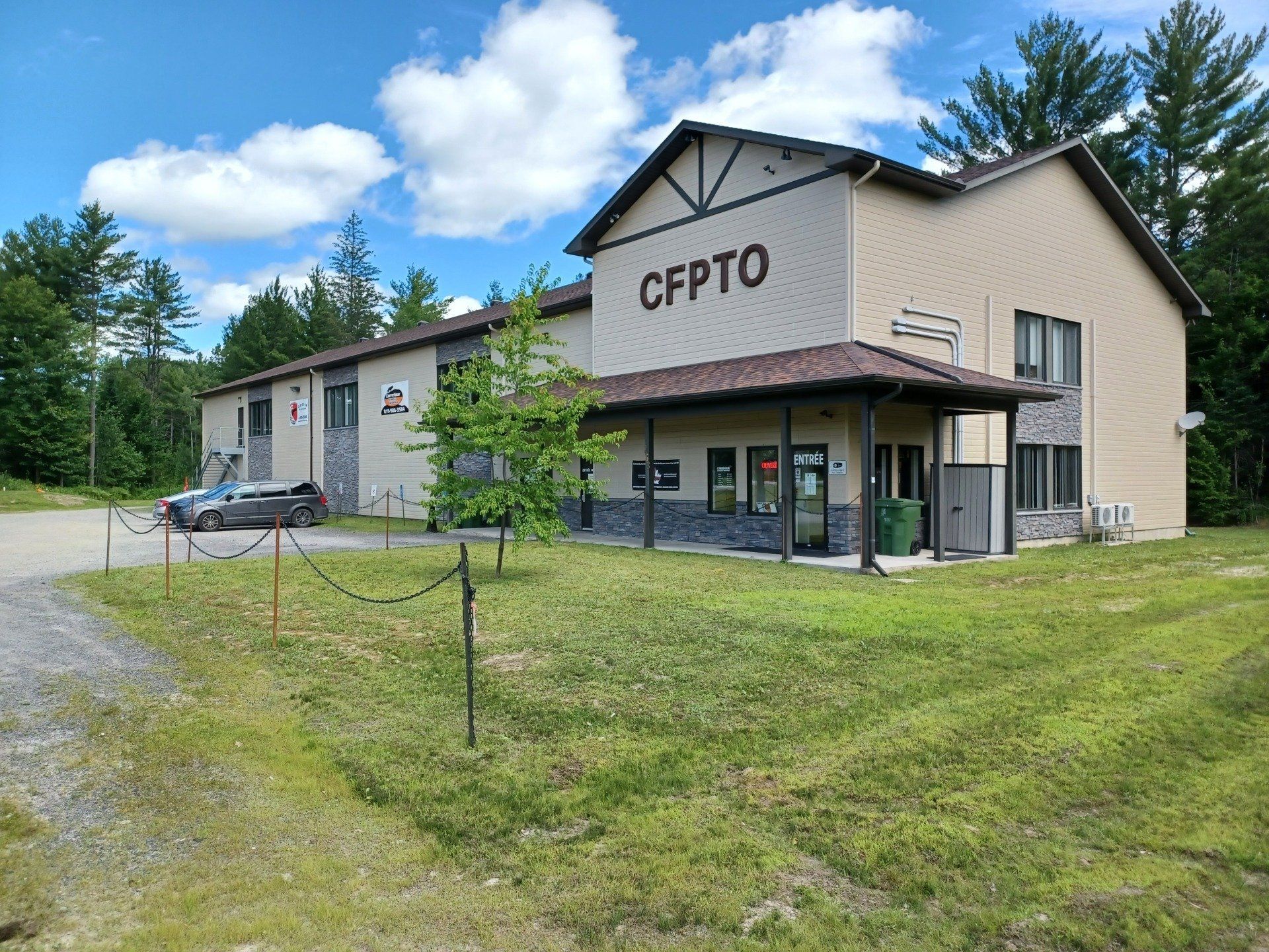 Bâtiment avec panneau « CFPTO » ; cour herbeuse, ciel couvert.