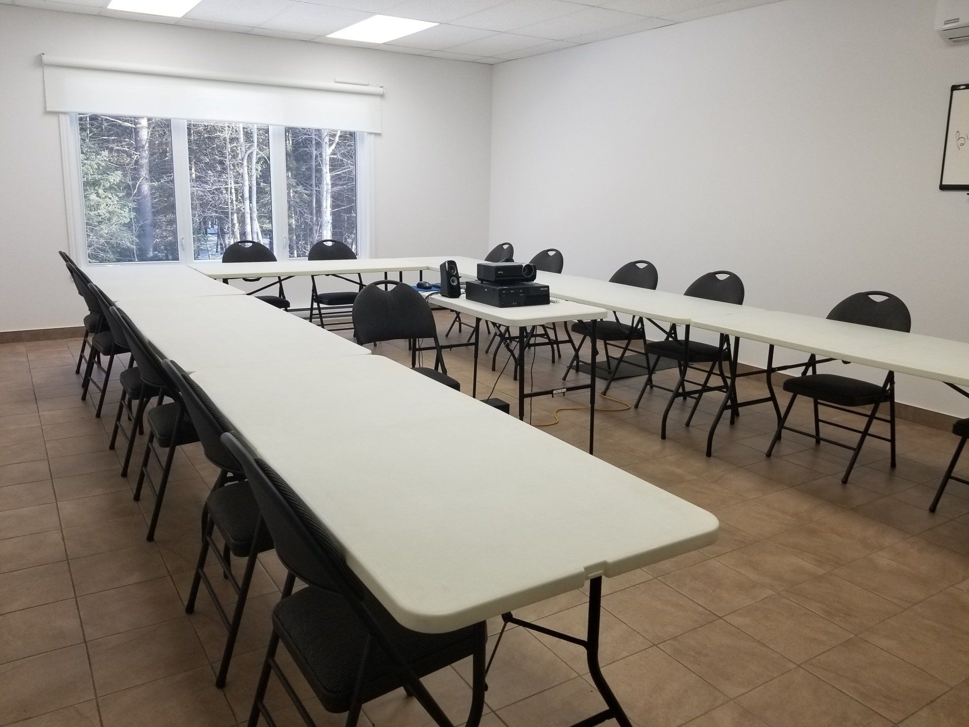 Une salle de classe avec une table en U et des chaises noires. Une fenêtre au fond laisse entrer la lumière naturelle.