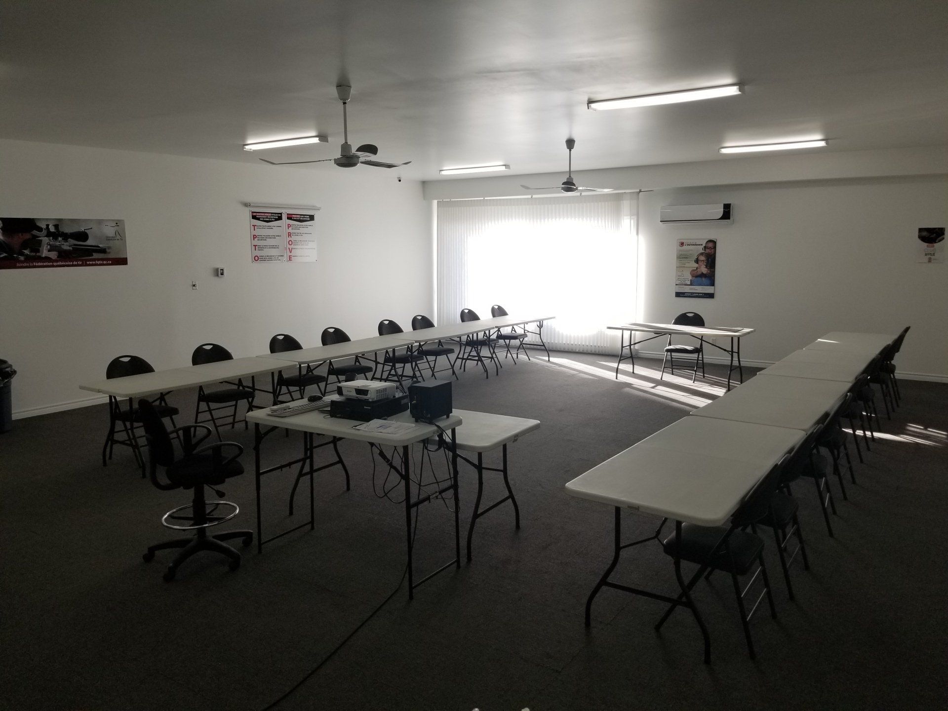 Salle de formation avec tables, chaises et projecteur. La lumière du soleil entre par une fenêtre.