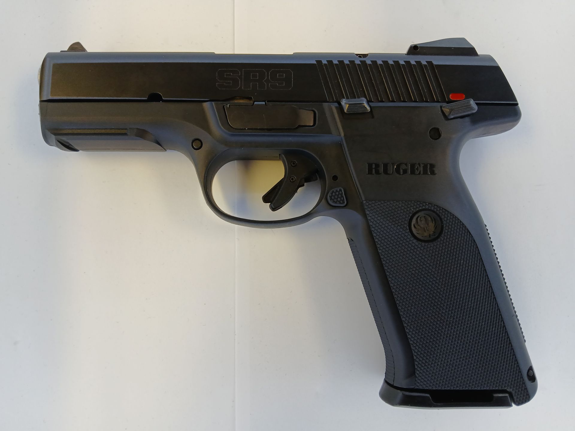 Pistolet Ruger SR9 noir avec poignée texturée, posé sur une surface blanche.