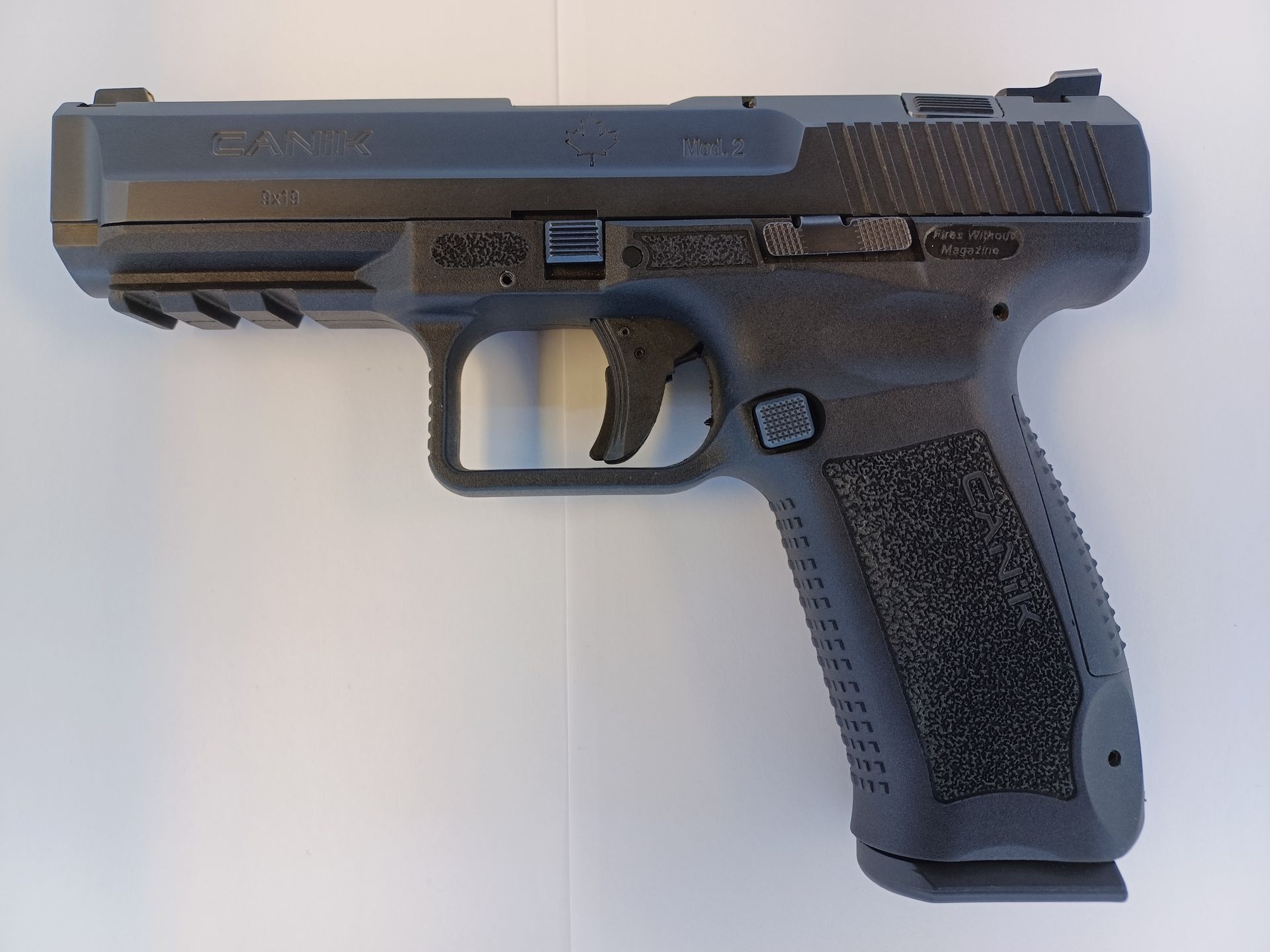 Pistolet semi-automatique noir sur une surface blanche, vu de côté.
