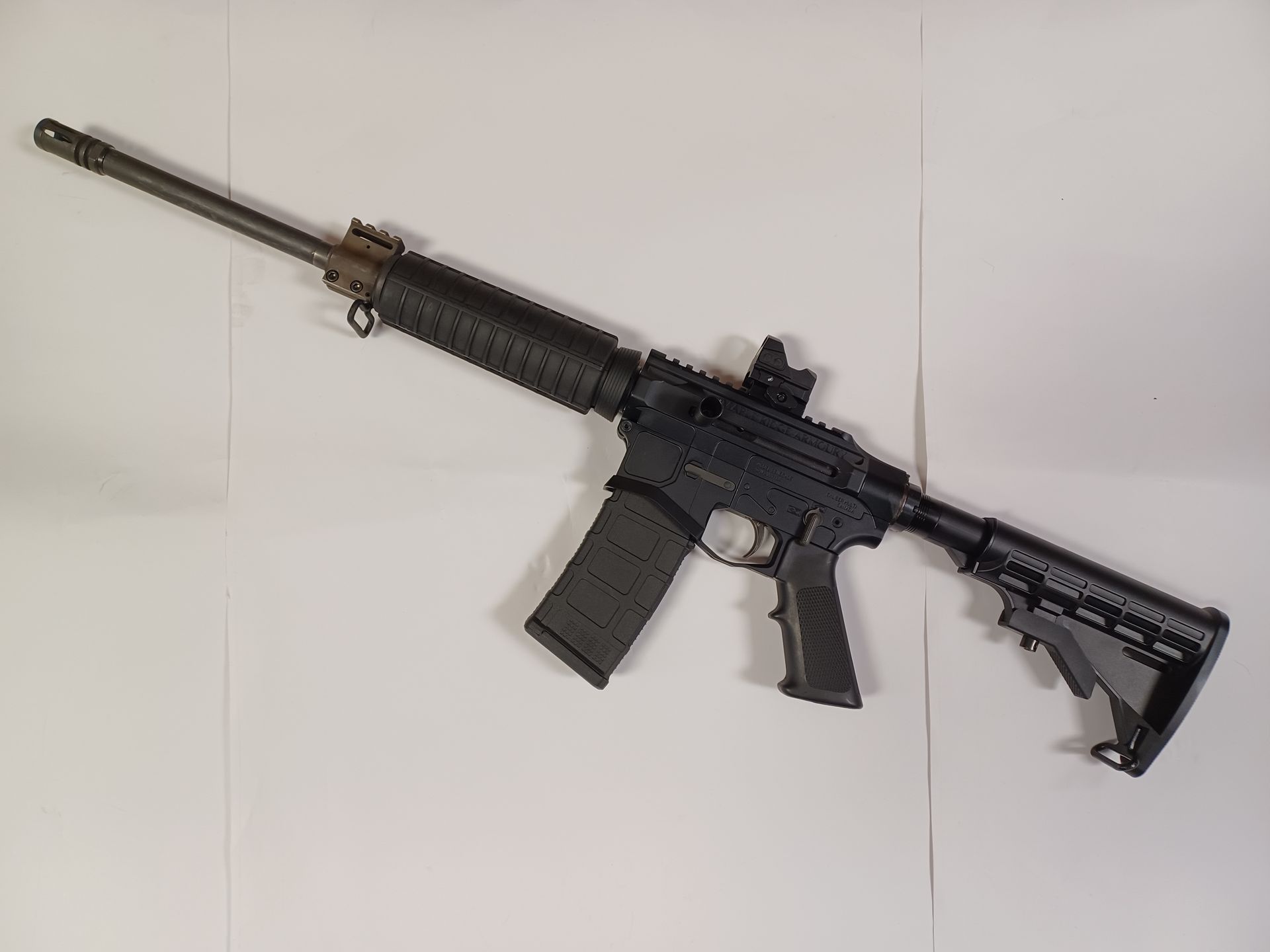 Fusil noir de style AR-15 avec une lunette et un chargeur, reposant sur un fond blanc.