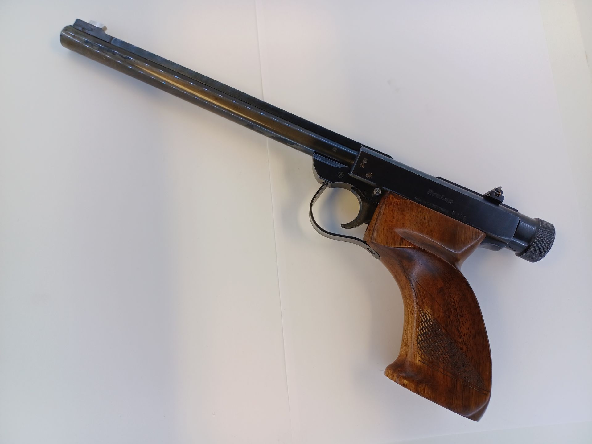 Pistolet à air comprimé avec poignée en bois, canon et cadre noirs, sur une surface blanche.