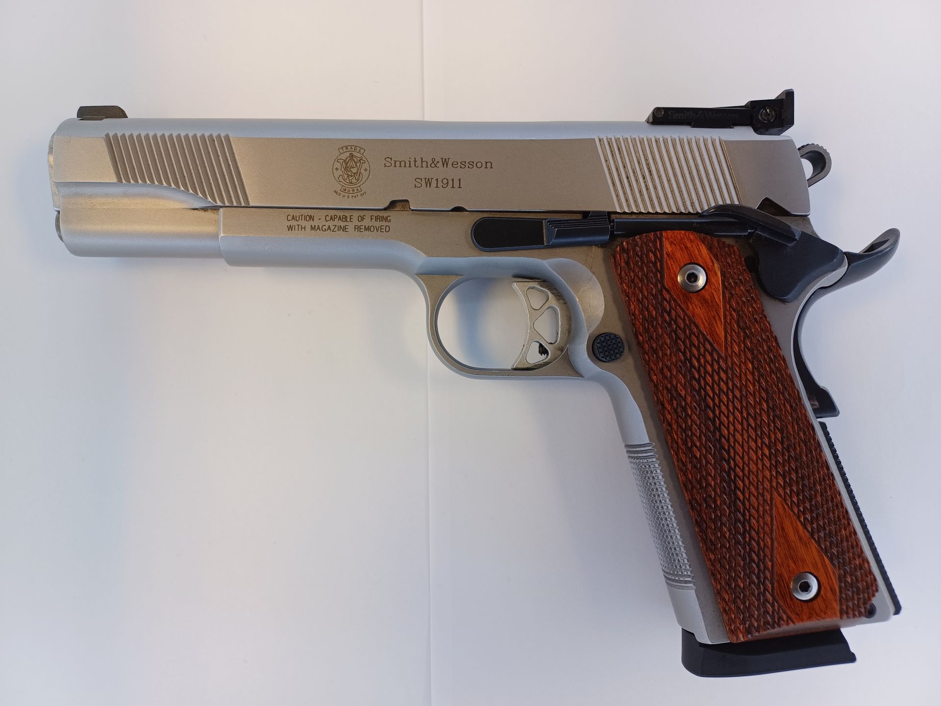 Pistolet Smith & Wesson 1911 en argent avec poignée en grain de bois sur fond blanc.