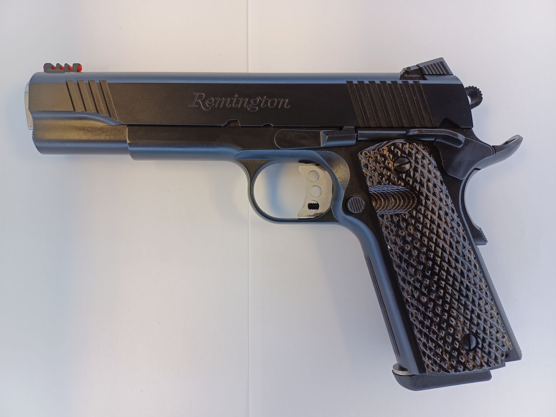 Pistolet Remington 1911 noir avec guidon rouge, posé sur une surface claire.