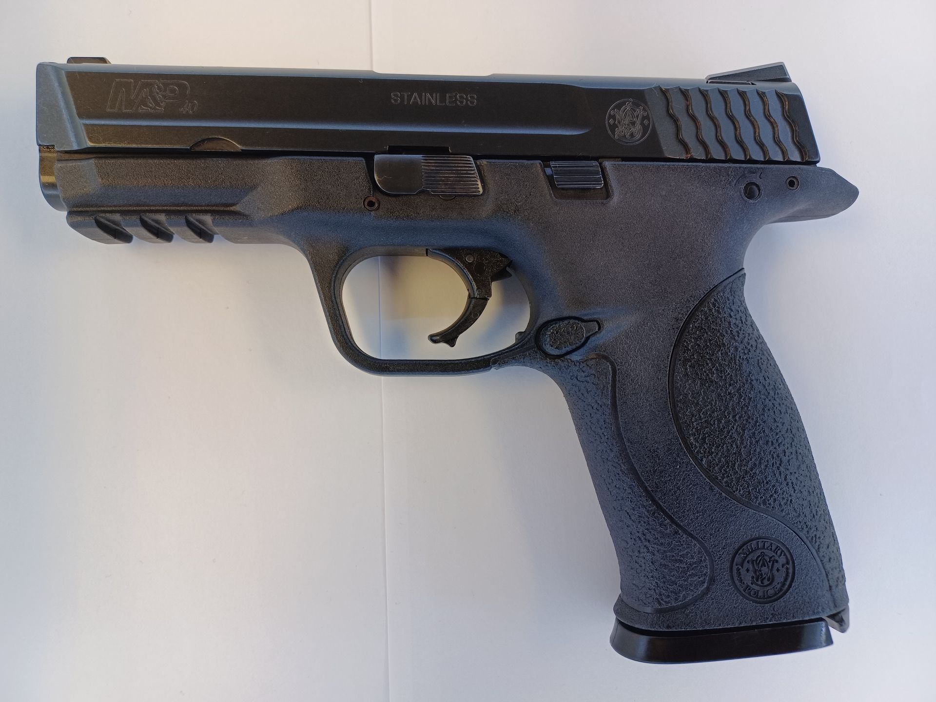 Pistolet noir sur une surface blanche, avec texture de poignée et marquages.