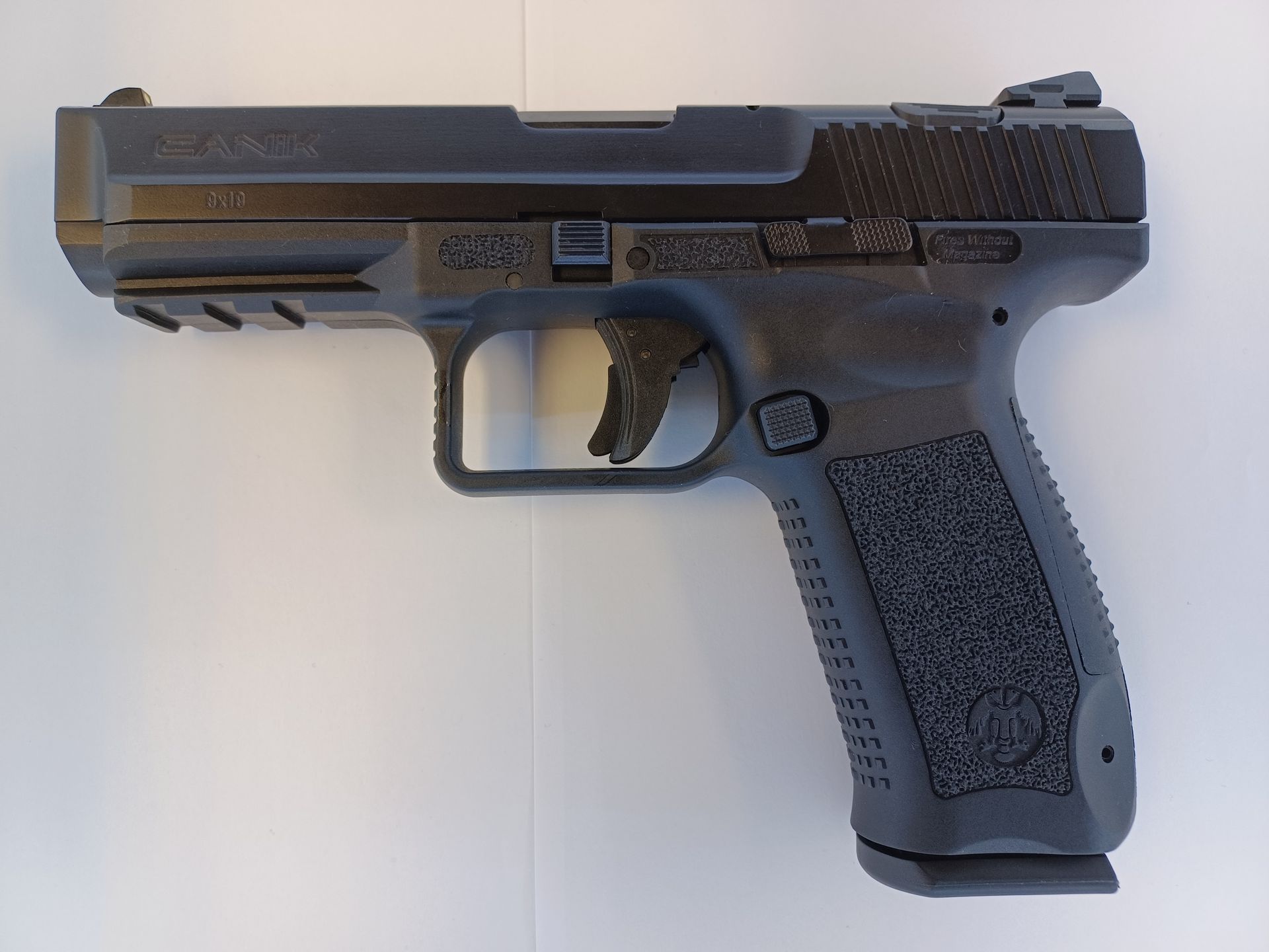 Pistolet semi-automatique noir sur une surface blanche, montrant les détails de la glissière, de la poignée et de la gâchette.