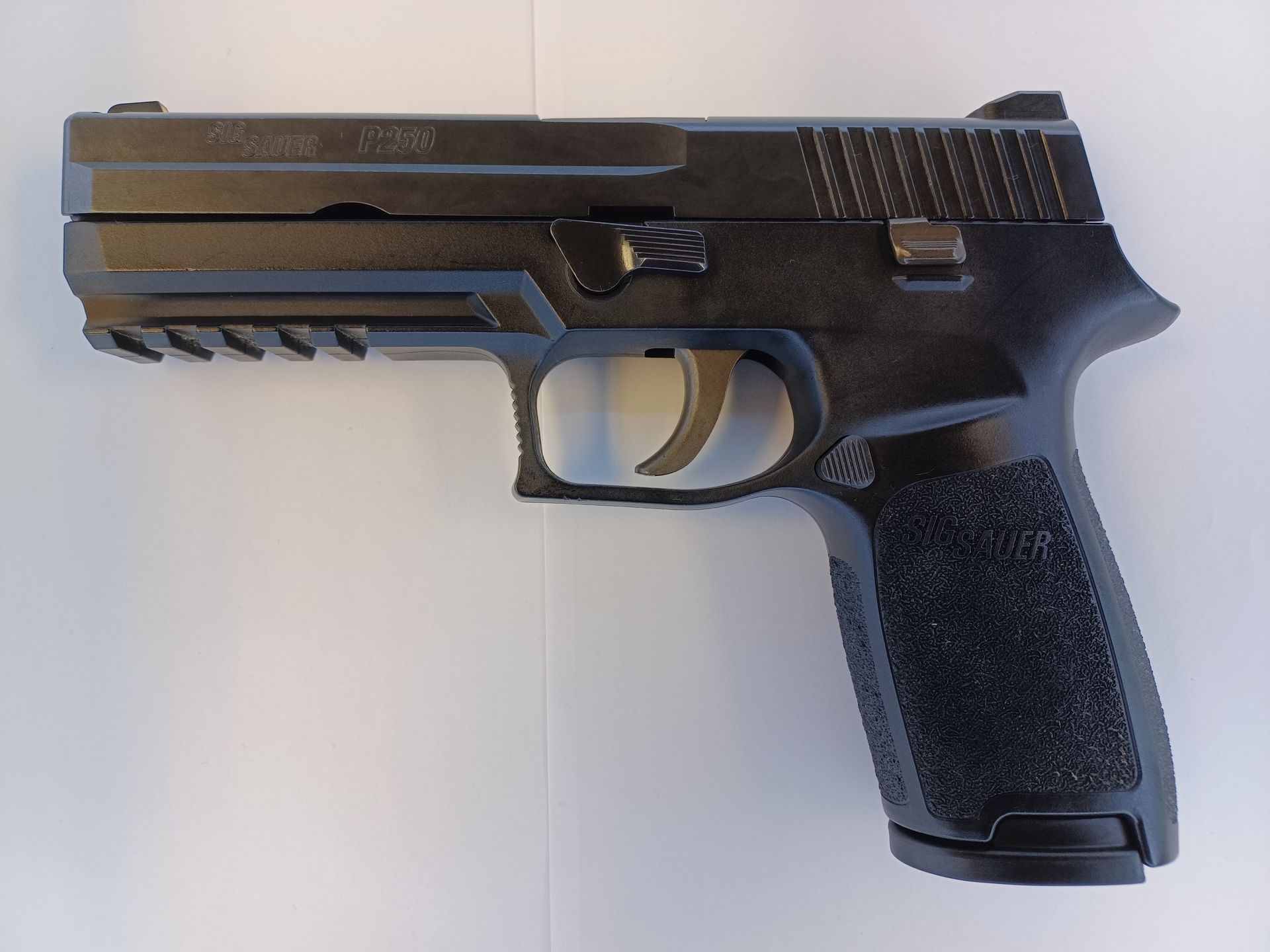 Pistolet Sig Sauer P320 noir, vue en angle, sur une surface blanche.