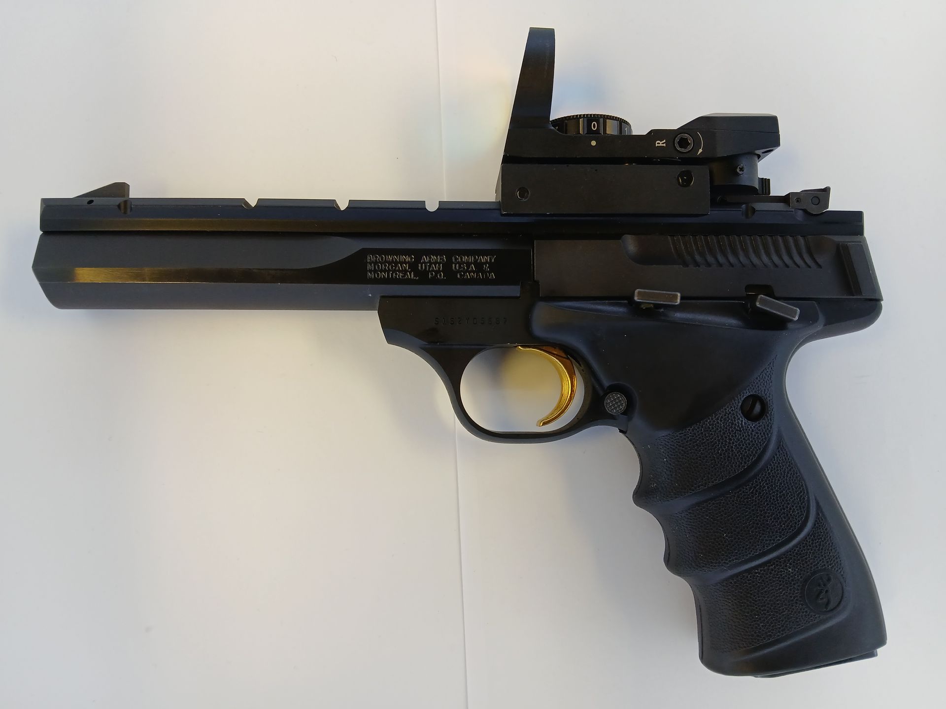 Pistolet noir avec viseur point rouge, gâchette dorée et poignée texturée.