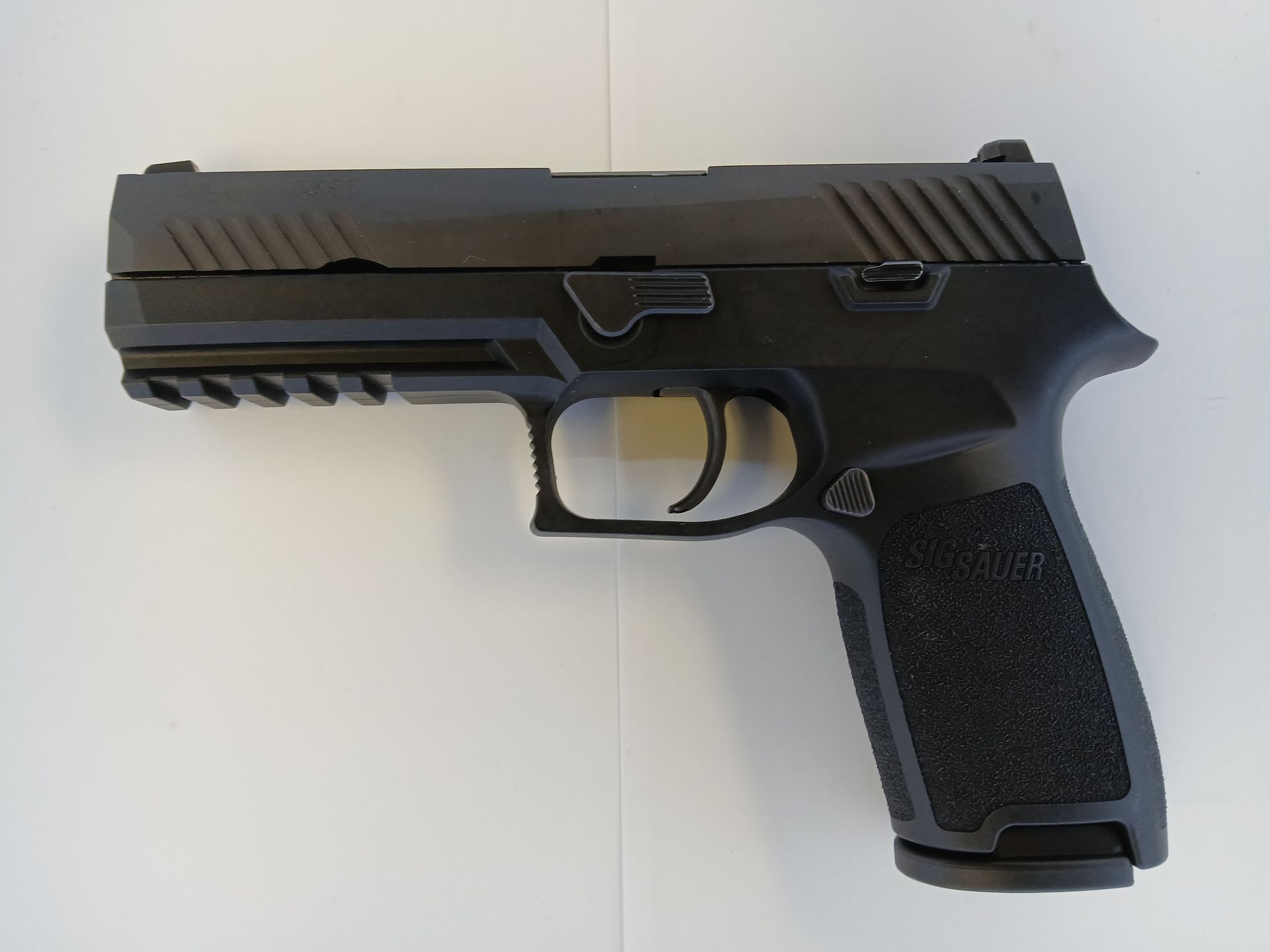 Pistolet semi-automatique noir sur une surface blanche ; le pistolet est vu de côté.