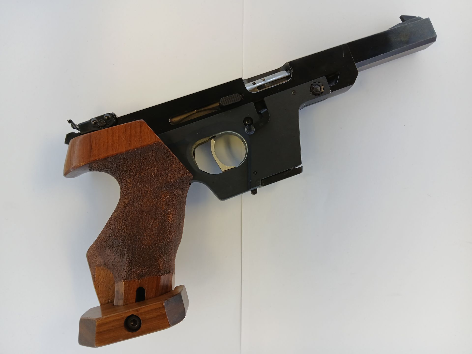 Pistolet cible, en métal noir avec poignée en bois, sur fond blanc.