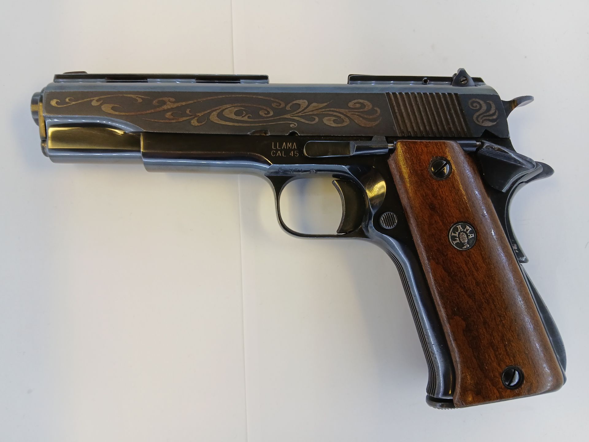 Pistolet foncé gravé avec poignées en bois sur fond blanc.