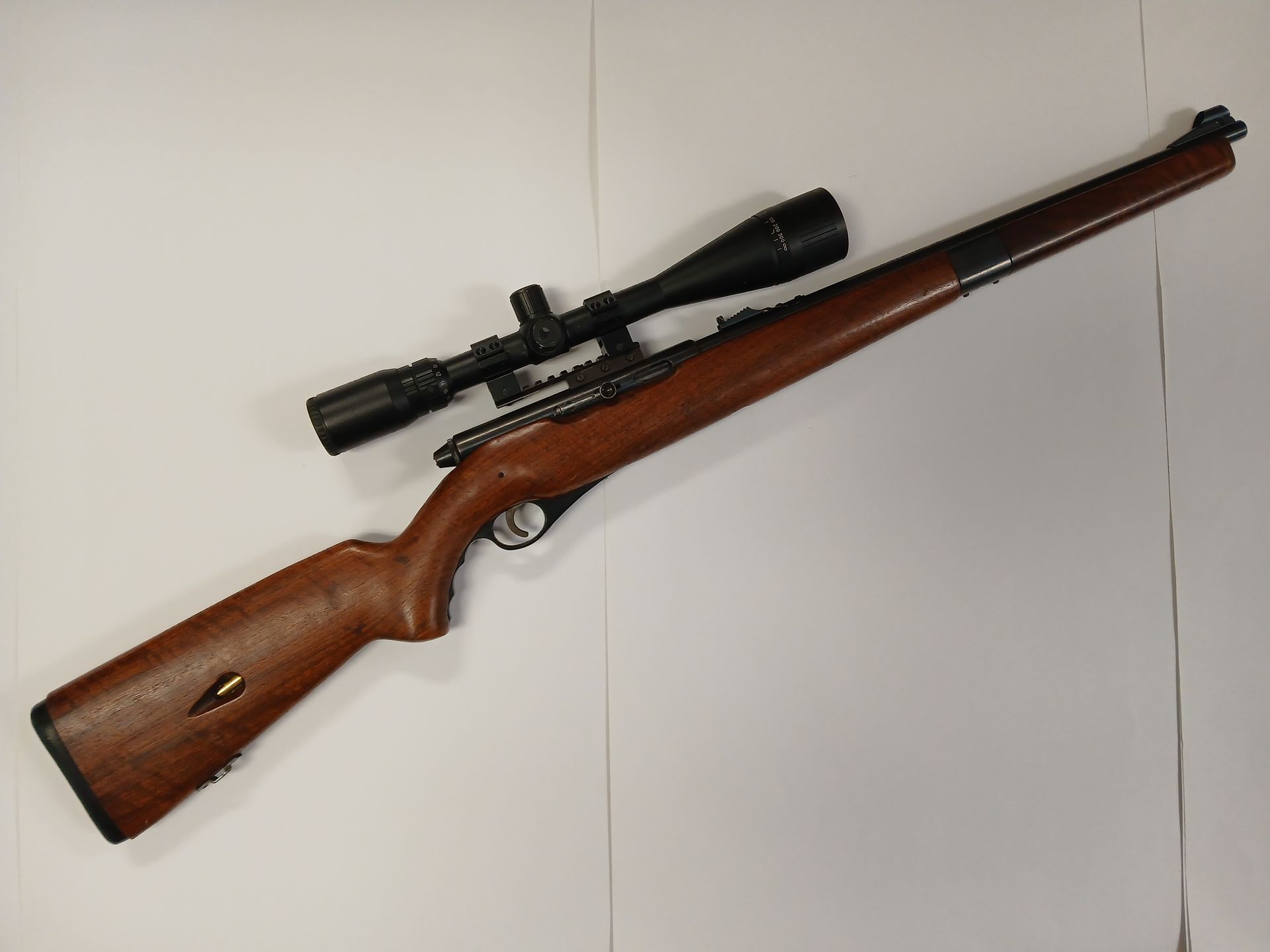 Fusil marron avec lunette, posé sur une surface blanche.
